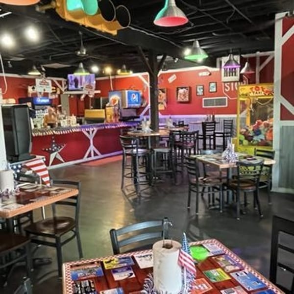 Casual restaurant interior with red walls, bar, tables, chairs, and arcade games.